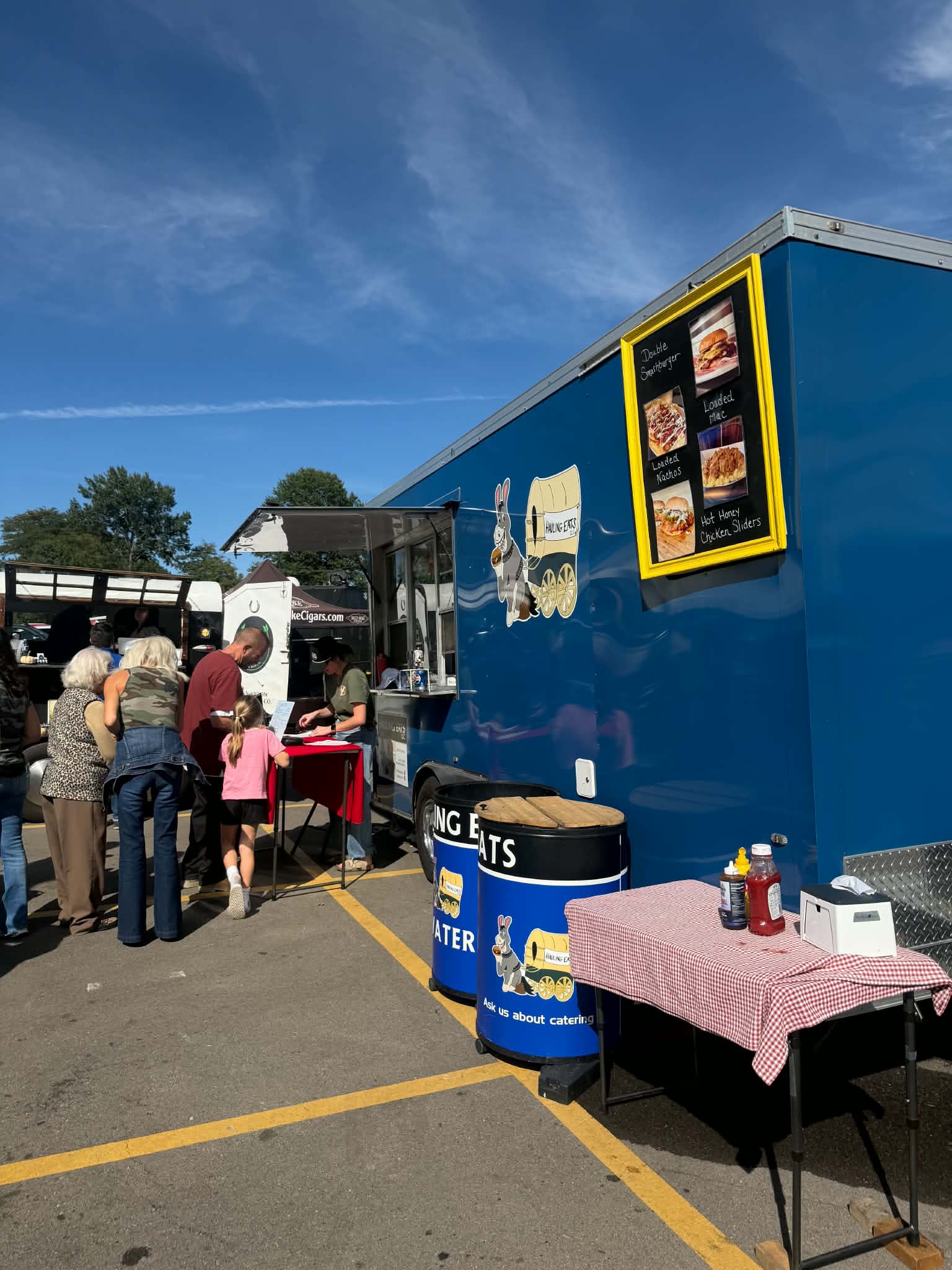 Families ordering at the Hauling Eats trailer window beside the photo menu board