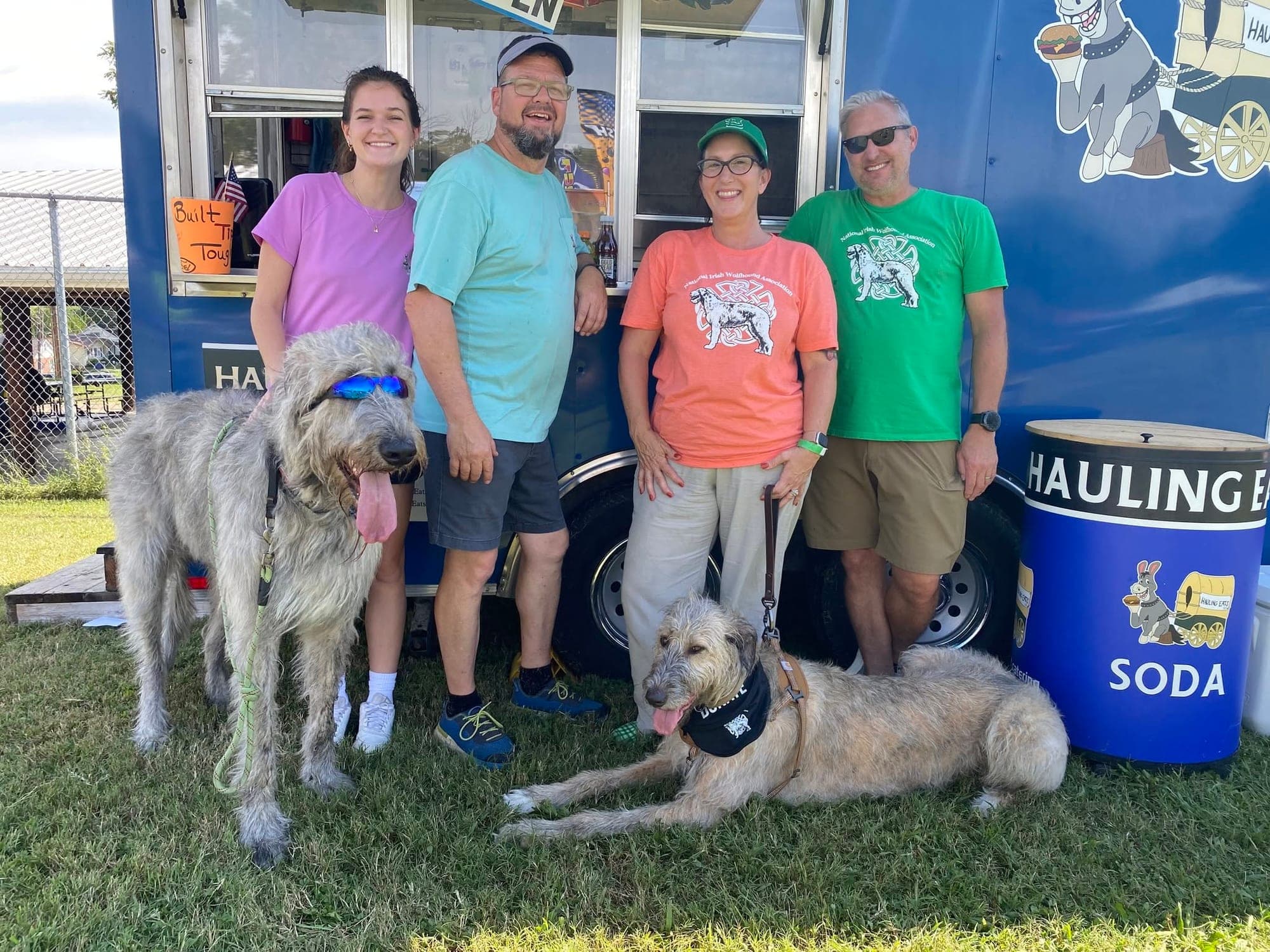 Four people and two Irish wolfhounds posing in front of the Hauling Eats trailer