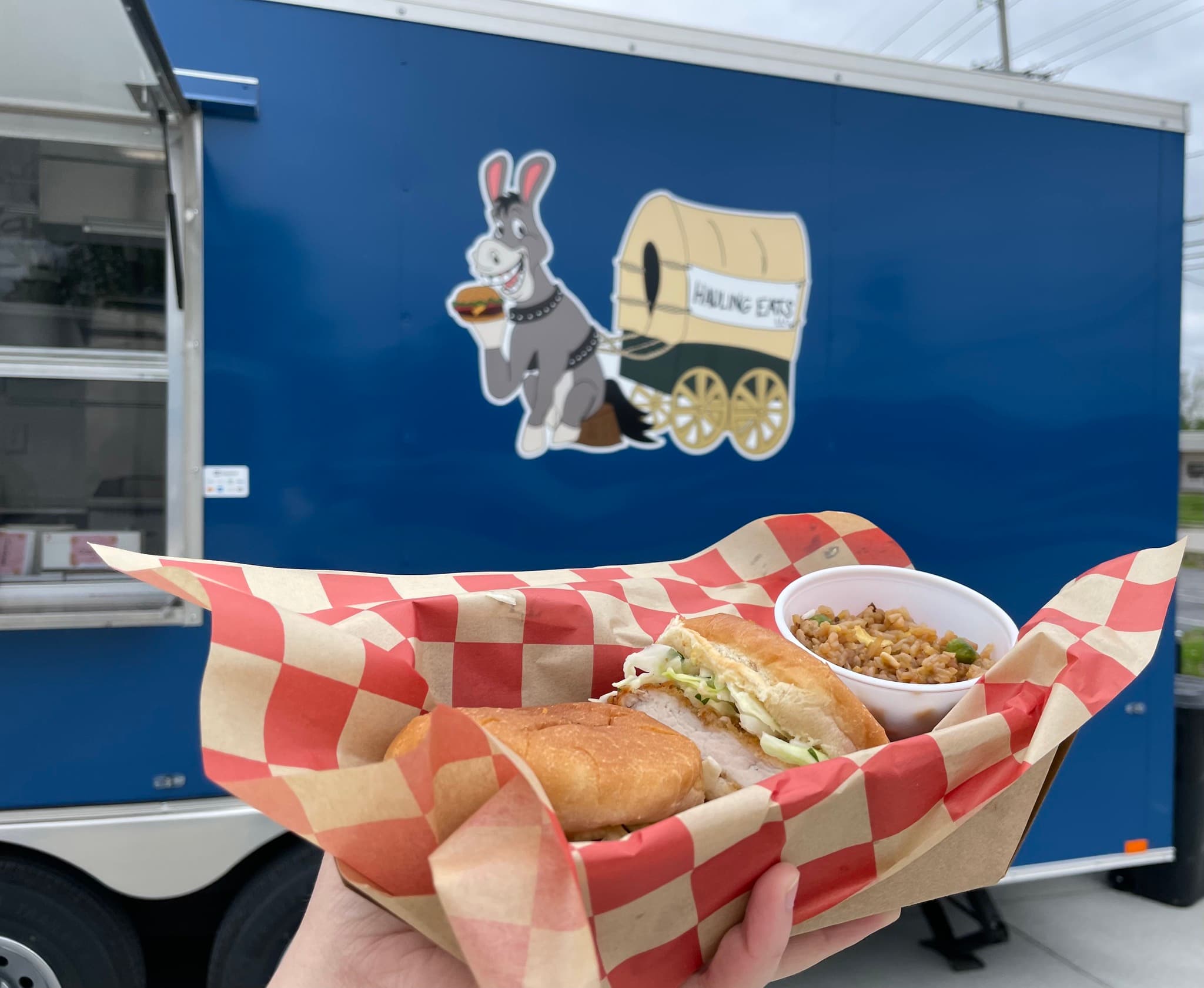 Chicken sandwich and fried rice in a red-checkered basket in front of the trailer