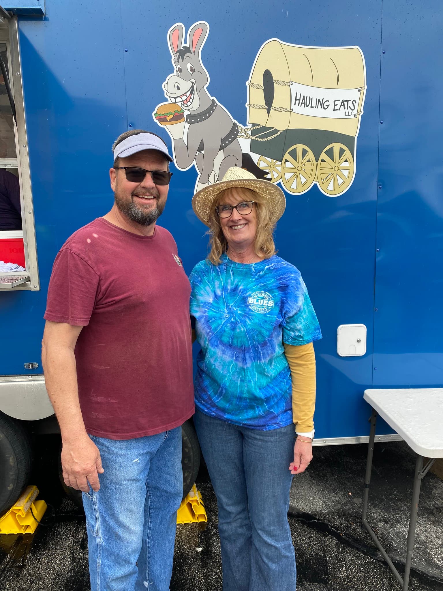The owners standing in front of the Hauling Eats trailer with the mule and wagon logo